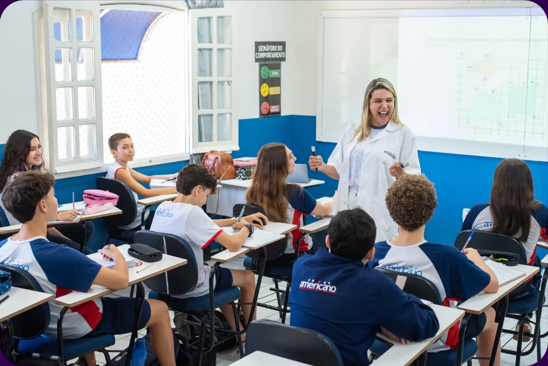 Professora sorrindo em sala de aula com alunos do Colégio Americano Guarapari